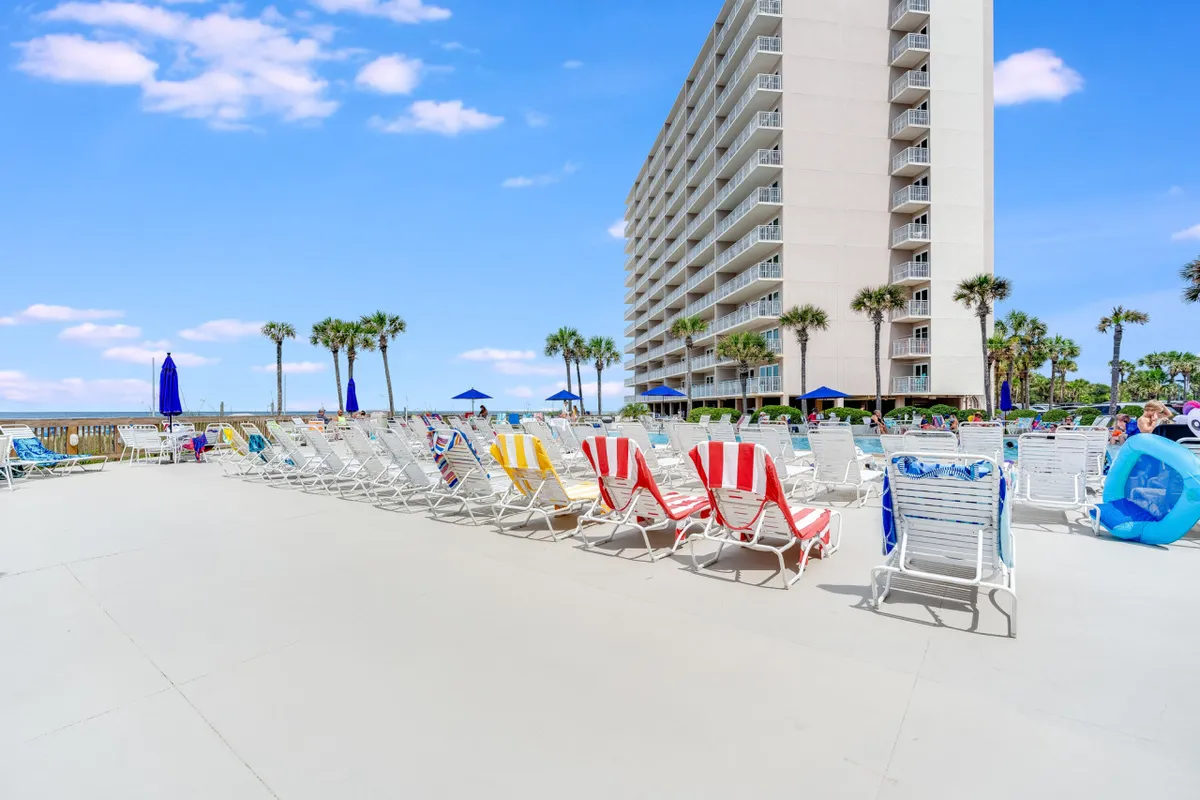 A lively exterior scene featuring a sparkling swimming pool, inviting lounge chairs, tall palm trees, and the Dunes of Panama high-rise building in the background. The pool area exudes a vacation-ready mood, ideal for swimming, sunbathing, and gathering with friends.