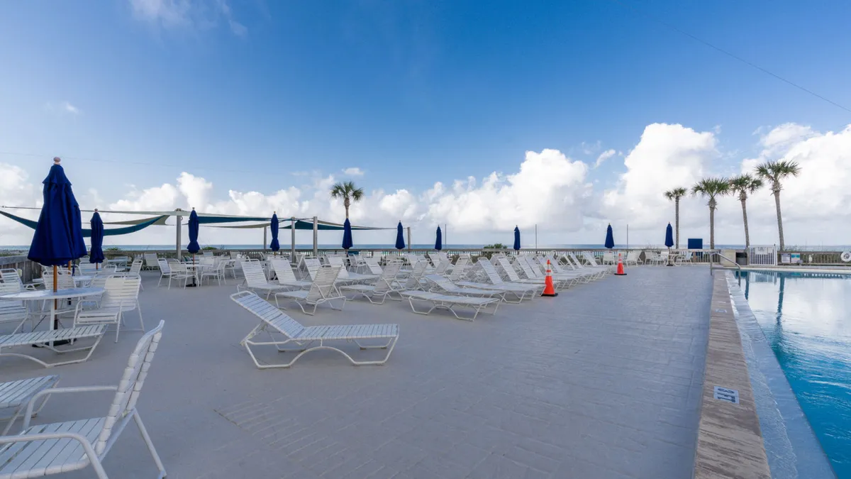 A sun-drenched pool deck lined with lounge chairs and umbrellas, with palm trees framing the sparkling pool. The inviting atmosphere is perfect for relaxation, socializing, or a swim—evoking the essence of resort leisure.