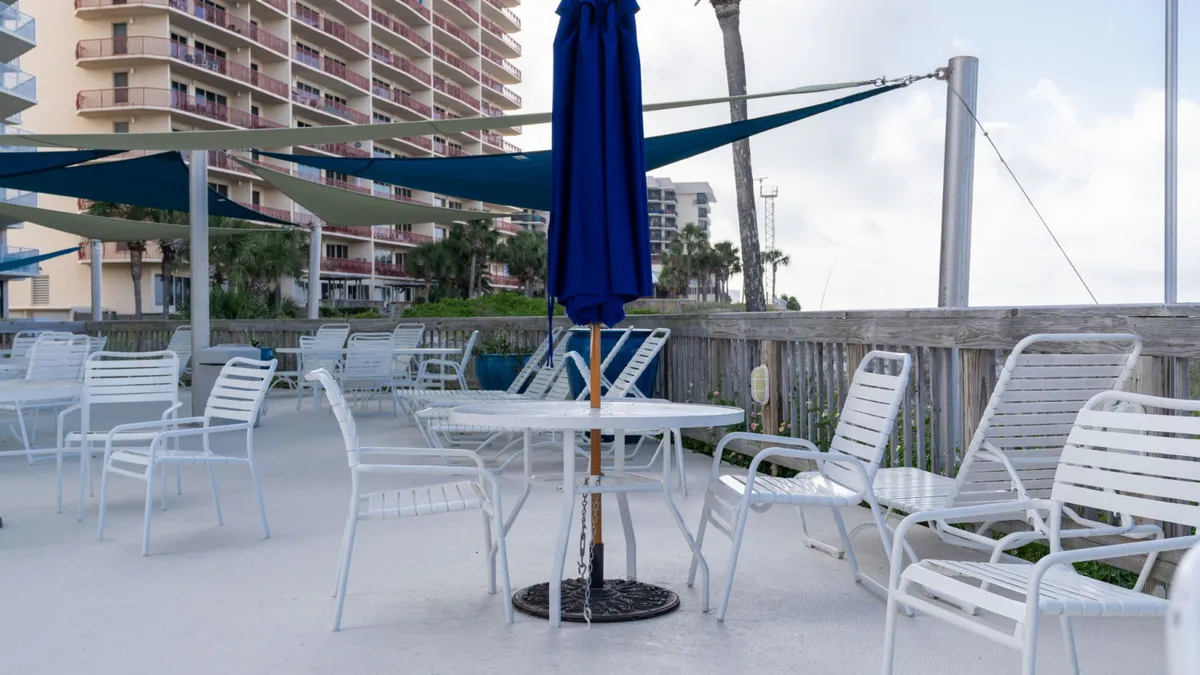 A shaded patio area with white chairs and a blue umbrella, set against the backdrop of the condo building. The setting is casual and comfortable, ideal for outdoor dining, morning coffee with an ocean breeze, or evening social gatherings.