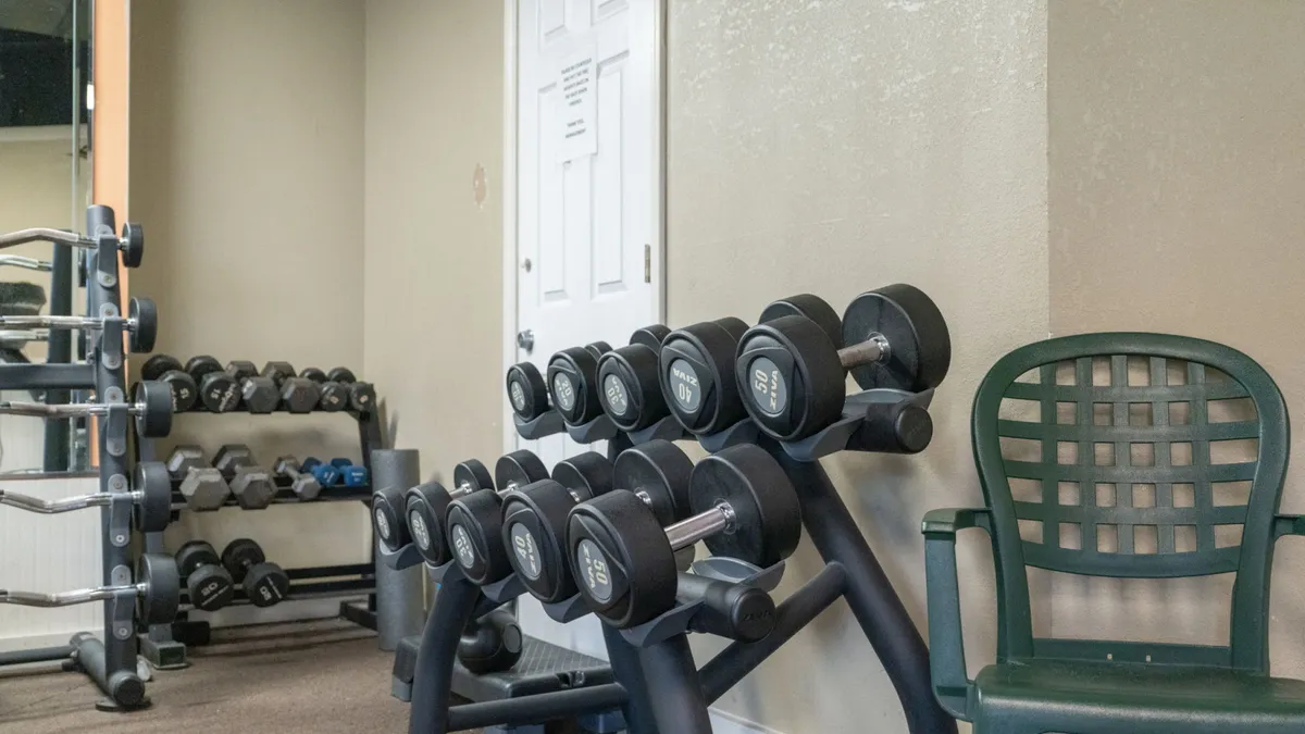 A motivating interior view of the fitness center, showcasing a well-equipped dumbbell rack and space for workouts. The setup is clean, modern, and designed for both solo and group fitness activities.