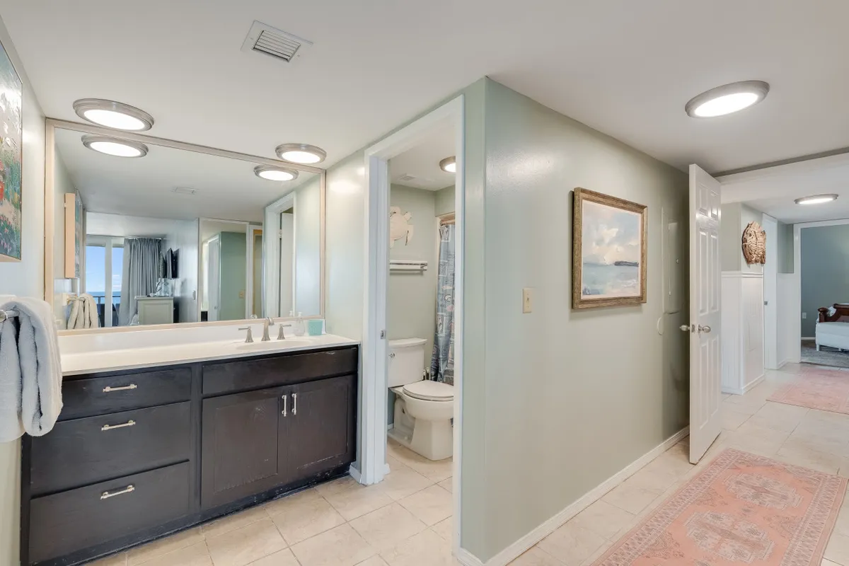 A modern bathroom featuring a double sink vanity, large mirror, framed artwork, and a visible shower area. The space feels calm and refreshing, designed for both morning routines and relaxing, end-of-day rituals.