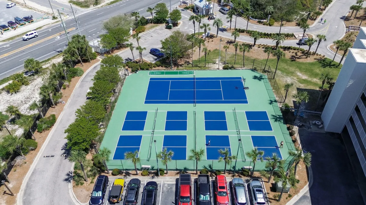 Tennis and pickleball courts with players engaged in games, bordered by a parking lot and greenery. The courts are bright and inviting, encouraging friendly competition and outdoor fun.